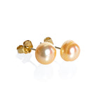 A product photo of simple peach-coloured pearl yellow gold earring studs on a white background.