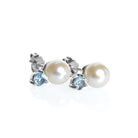 A product photo of delicate white pearl earring studs on a white background. The white pearls each have aquamarine detailing above them connecting to the white gold studs.