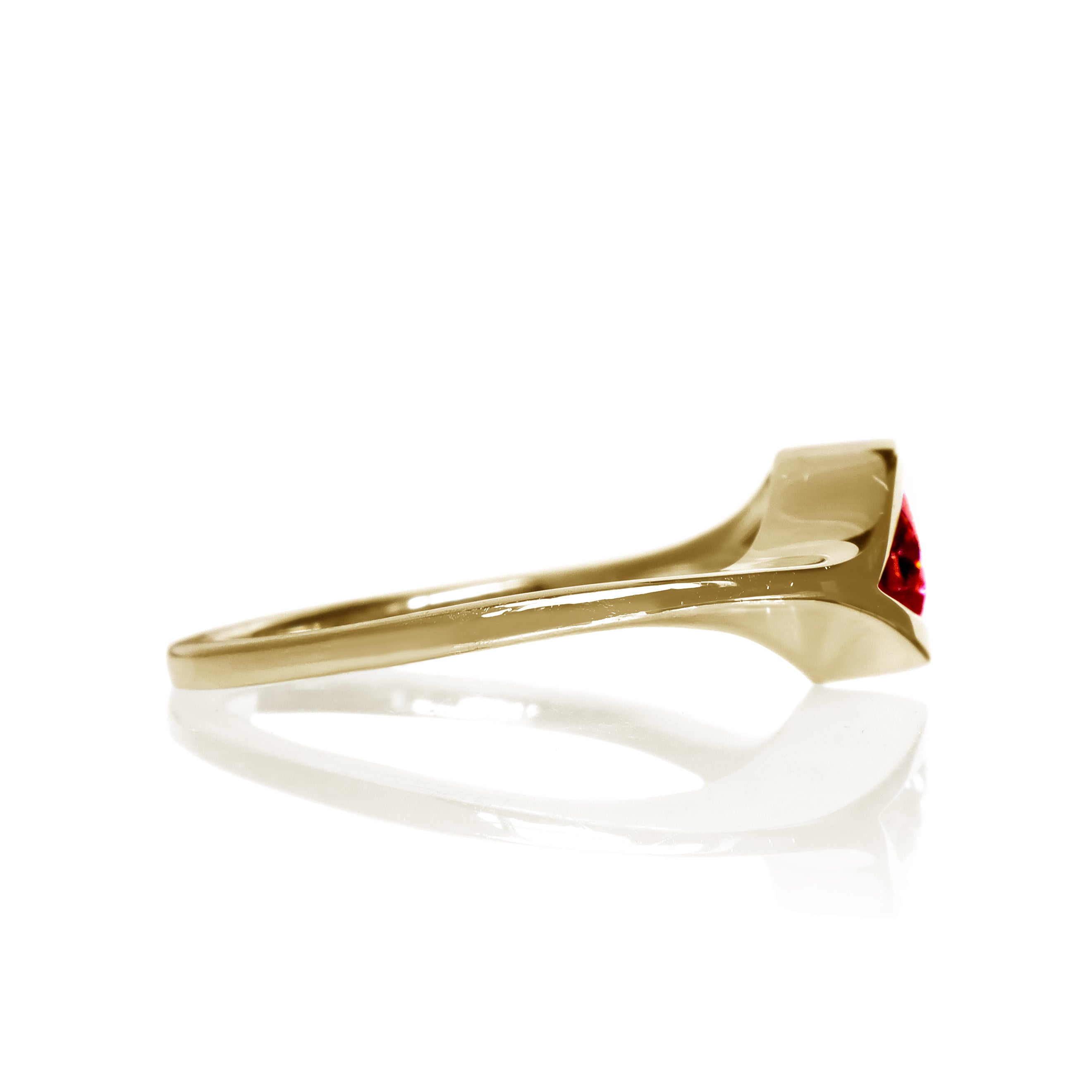A product photo of a Round Garnet Ring in 9k Yellow Gold sitting on a plain white background. The 5.5mm garnet sits in the centre, and a simple golden band splits on either side of the jewel, meeting above and below, holding it in place like the corners of an eye. The stone is a deep red, reflecting sanguine hues across its multi-faceted edges.