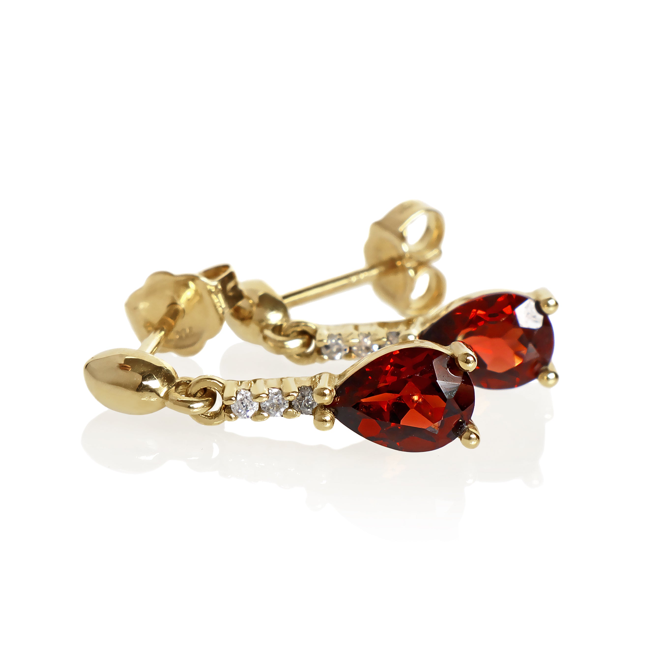 A product photo of 7x5mm Pear Garnet & Diamond Earrings in 9k Yellow Gold sitting on a plain white background. A golden strip connects the garnets to the studs, each strip adorned with 3 diamonds each. The garnets reflect sanguine hues across their multi-faceted edges.