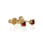 A product photo of 3.5mm Round Garnet Earring Studs in 9k Yellow Gold sitting on a plain white background. The stones are held in place by 4 delicate golden claws arranged in a flower-like pattern where they meet the stud. The garnets reflect sanguine hues across their multi-faceted edges.