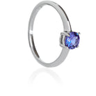 A product photo of a white gold tanzanite solitaire ring sitting on a white background. The band is smooth and simple, with the centre stone held in place by 4 small claws. The deep blue tanzanite stone reflects violet blue and indigo colours from its many edges.