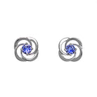 A product photo of white gold stud tanzanite earrings sitting on a white background. The small stones are framed by ornate, flowery white gold backs. The deep blue tanzanite stones reflect violet blue and indigo light from their many edges.