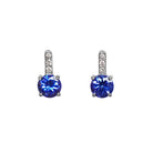 A product photo of white gold tanzanite stud earrings sitting on a white background. A golden strip connects the round stones to the studs, each strip adorned with 3 diamonds each. The deep blue tanzanite stones reflect violet blue and indigo light from their many edges.