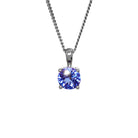 A product photo of a white gold tanzanite pendant suspended by a chain against a white background. The round stone is held in place by 4 small claws, and reflects violet blue and indigo colours from its many edges.