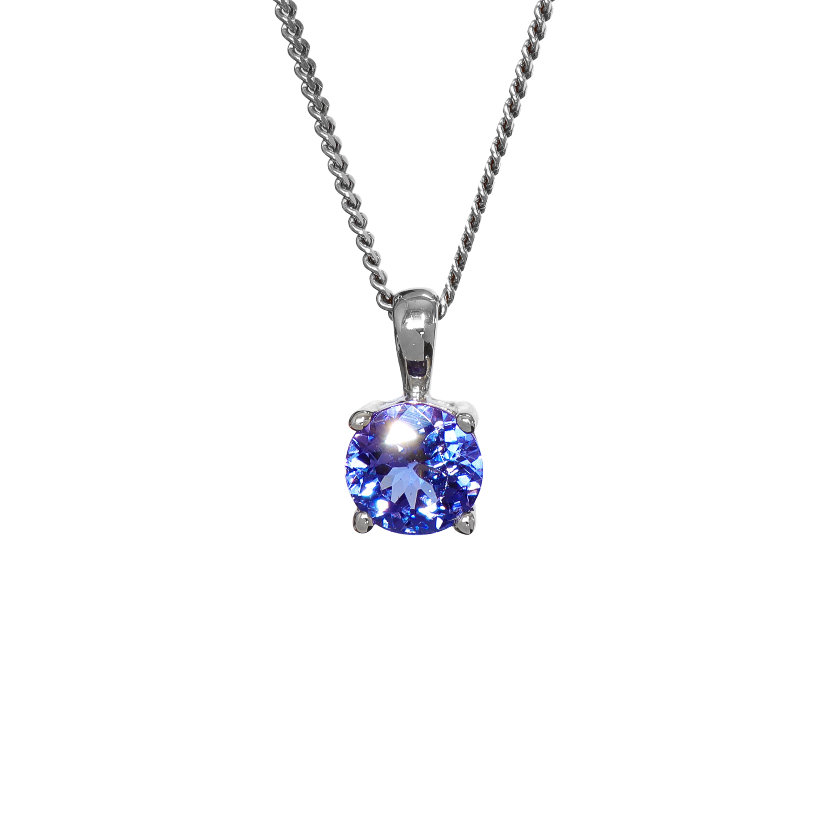 A product photo of a white gold tanzanite pendant suspended by a chain against a white background. The round stone is held in place by 4 small claws, and reflects violet blue and indigo colours from its many edges.