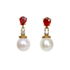 A product photo of a pair of ornate pearl drop stud earrings in yellow gold suspended over a white background. The pearls are creamy white and round, with one small diamond followed by a pear-shaped ruby on each piece linking them to the back of the golden stud.