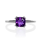 A product photo of a white gold ring with a large cushion-cut amethyst centre stone on a white background. The band is smooth gold, and the deep purple amethyst centre stone is held in place by 8 little claws, 2 on each corner.