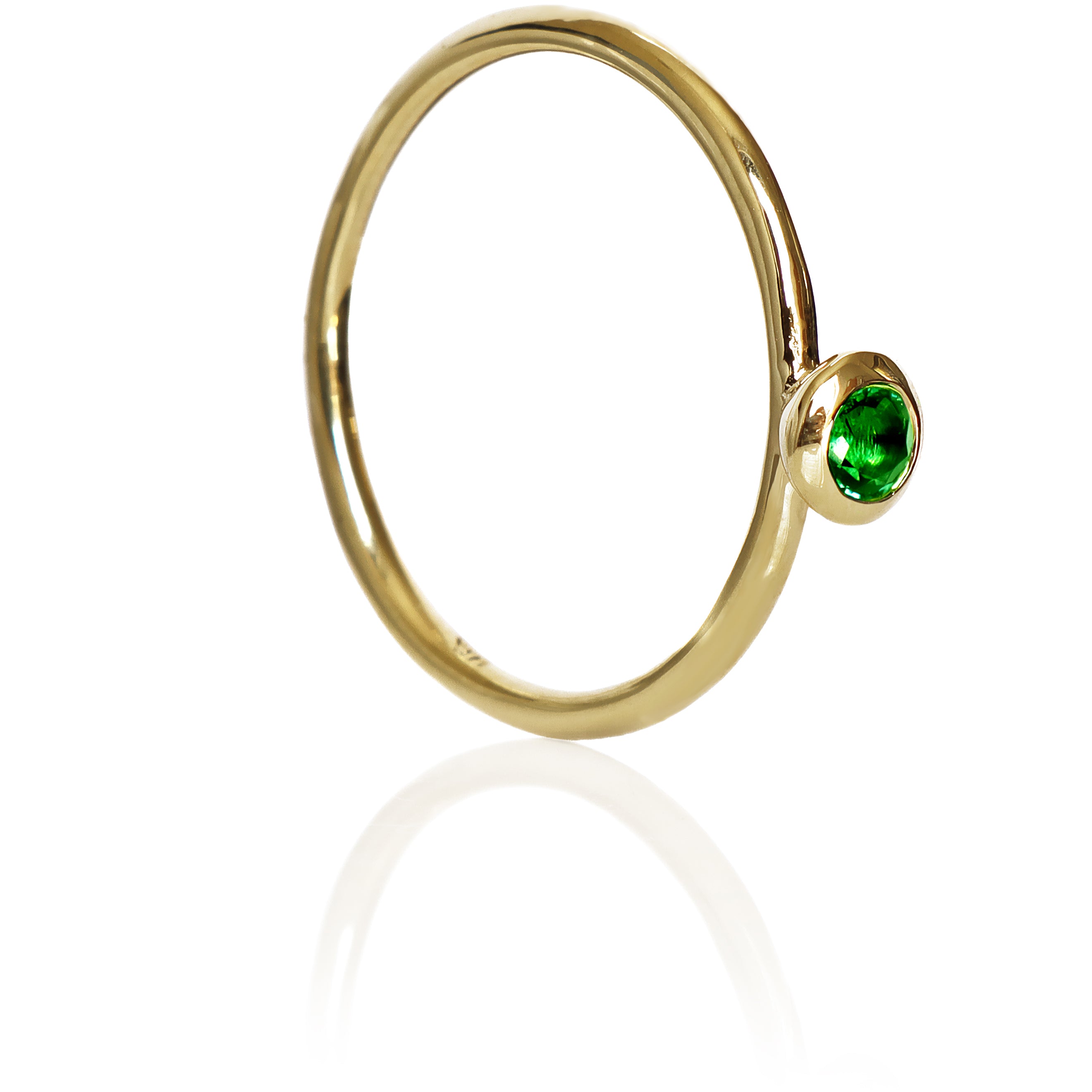 A product photo of a delicate yellow gold stacking ring with a tiny, bezel-set tsavorite in the centre sitting on a white background. The band is slim and thread-like, with the focus drawn to the petite 3mm glinting green centre stone.