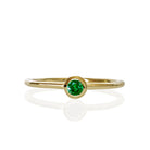 A product photo of a delicate yellow gold stacking ring with a tiny, bezel-set tsavorite in the centre sitting on a white background. The band is slim and thread-like, with the focus drawn to the petite 3mm glinting green centre stone.