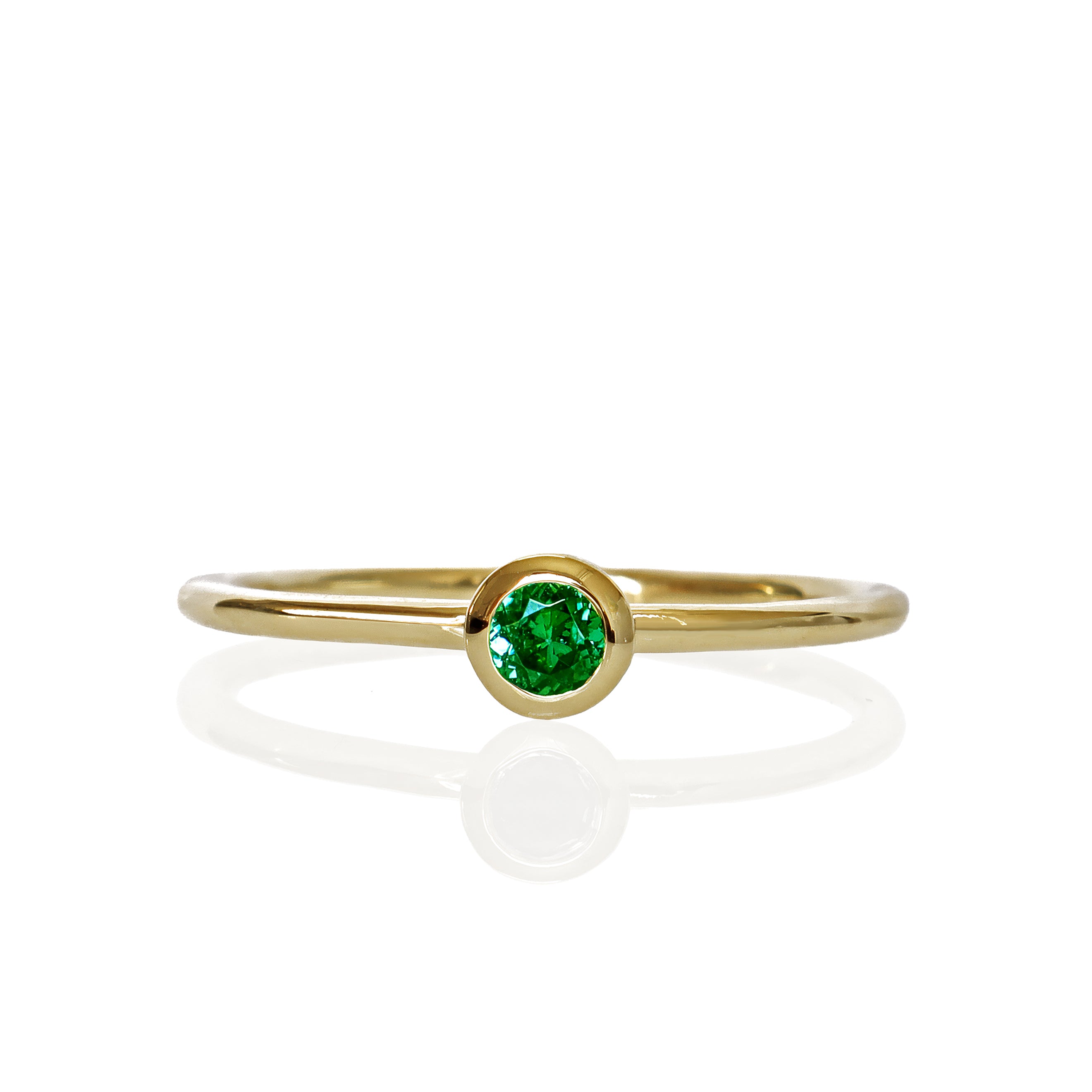 A product photo of a delicate yellow gold stacking ring with a tiny, bezel-set tsavorite in the centre sitting on a white background. The band is slim and thread-like, with the focus drawn to the petite 3mm glinting green centre stone.