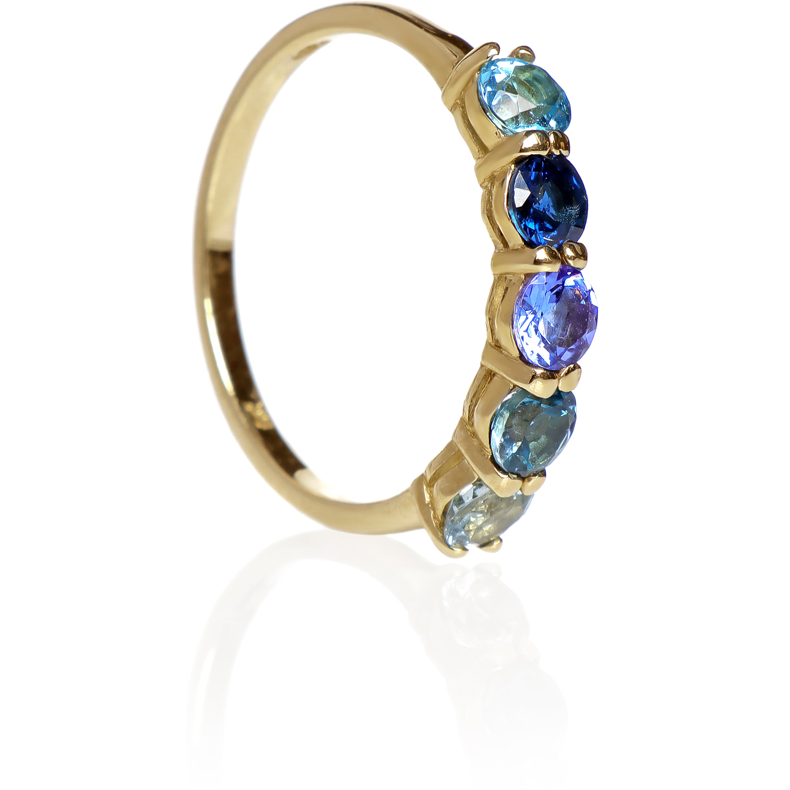 A product photo of a bold, multi-gemstone ring in 9k yellow gold – made up of 5 blue coloured jewels – sitting on a white background. From left to right, 4.5mm round-cut aquamarine, blue tourmaline, tanzanite, sapphire and blue topaz stones make up a bold statement piece.