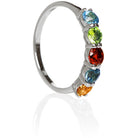 A product photo of a bold, multi-gemstone ring in 9k yellow gold – made up of rainbow-coloured jewels – sitting on a white background. From left to right, 4.5mm round-cut citrine, london blue topaz, red garnet, peridot and blue topaz.