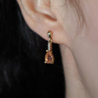 A product photo of 7x5mm Pear Morganite & Diamond Earrings in 9k Yellow Gold sitting on a plain white background. A golden strip connects the morganites to the studs, each strip adorned with 3 diamonds each. The morganites reflect light pinky hues across their multi-faceted edges.