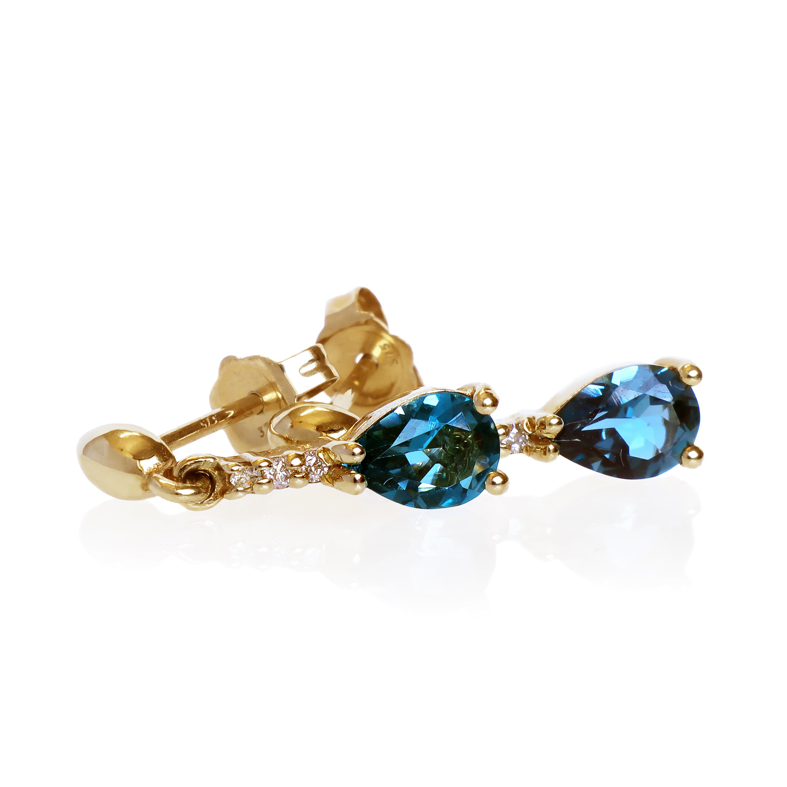 A product photo of 7x5mm Pear London Blue Topaz & Diamond Earrings in 9k Yellow Gold sitting on a plain white background. A golden strip connects the stones to the studs, each strip adorned with 3 diamonds each. The stones reflect deep, oceanic hues across their multi-faceted edges.