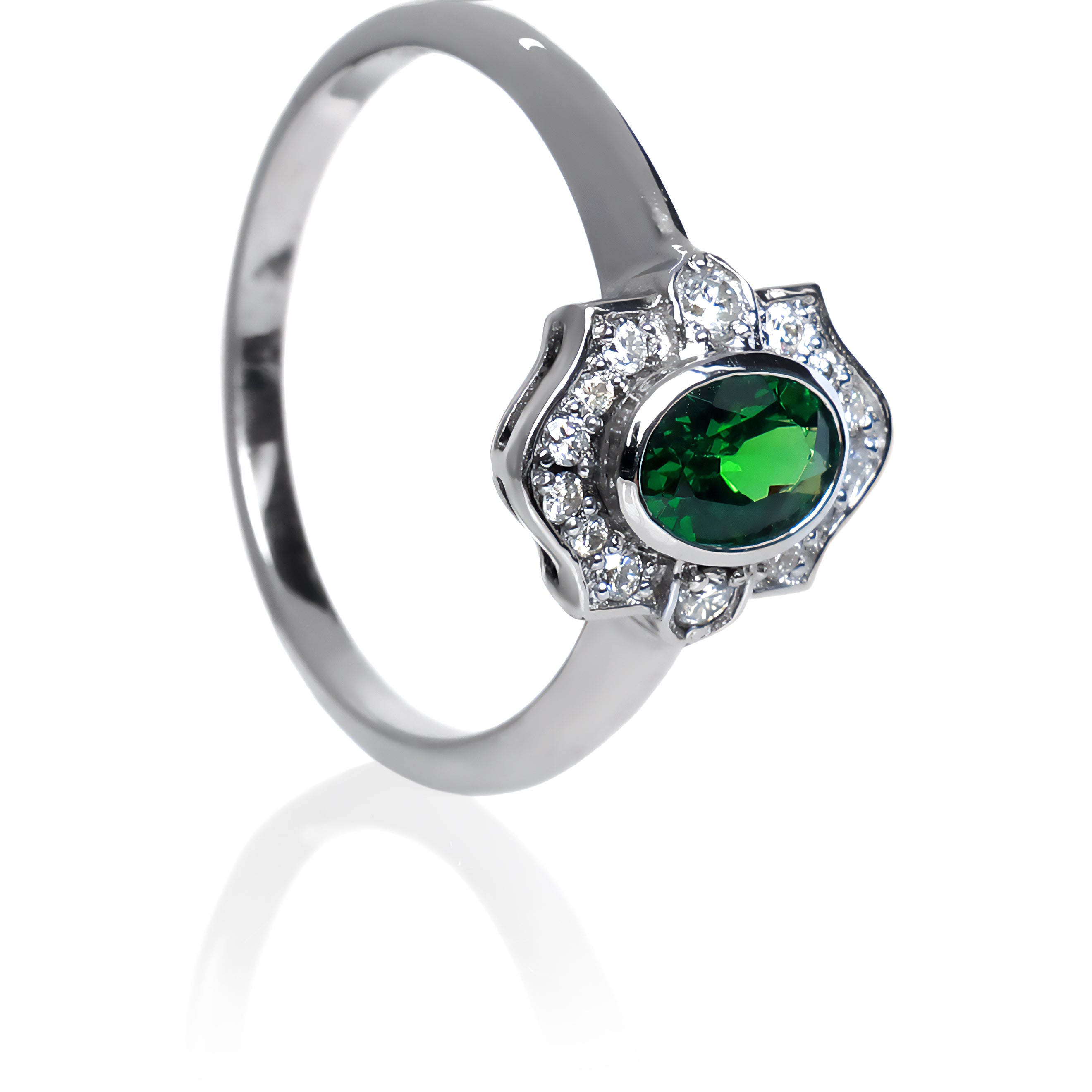 A product photo of a vintage-styled tsavorite and diamond ring in 9k white gold on a white background. The oval-shaped tsavorite is held in place by a bezel setting, and is surrounded by an ornate white gold frame embedded with diamonds, reminiscent of vintage jewellery styles of the past. The green gemstone colour would be a good emerald substitute. 
