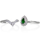 A product photo of a bridal/wedding set made of solid 9k white gold. The engagement ring is made up of a pear-shaped tsavorite gemstone, framed by a halo of diamonds and elegant gold detailing. The band is rounded and smooth, making for comfortable wear. The wedding band is designed to match the engagement ring perfectly, with 10 diamonds embedded along its length to echo the halo that frames the engagement ring's stone. The green gemstone colour would be a good emerald alternative for wearers born in May.