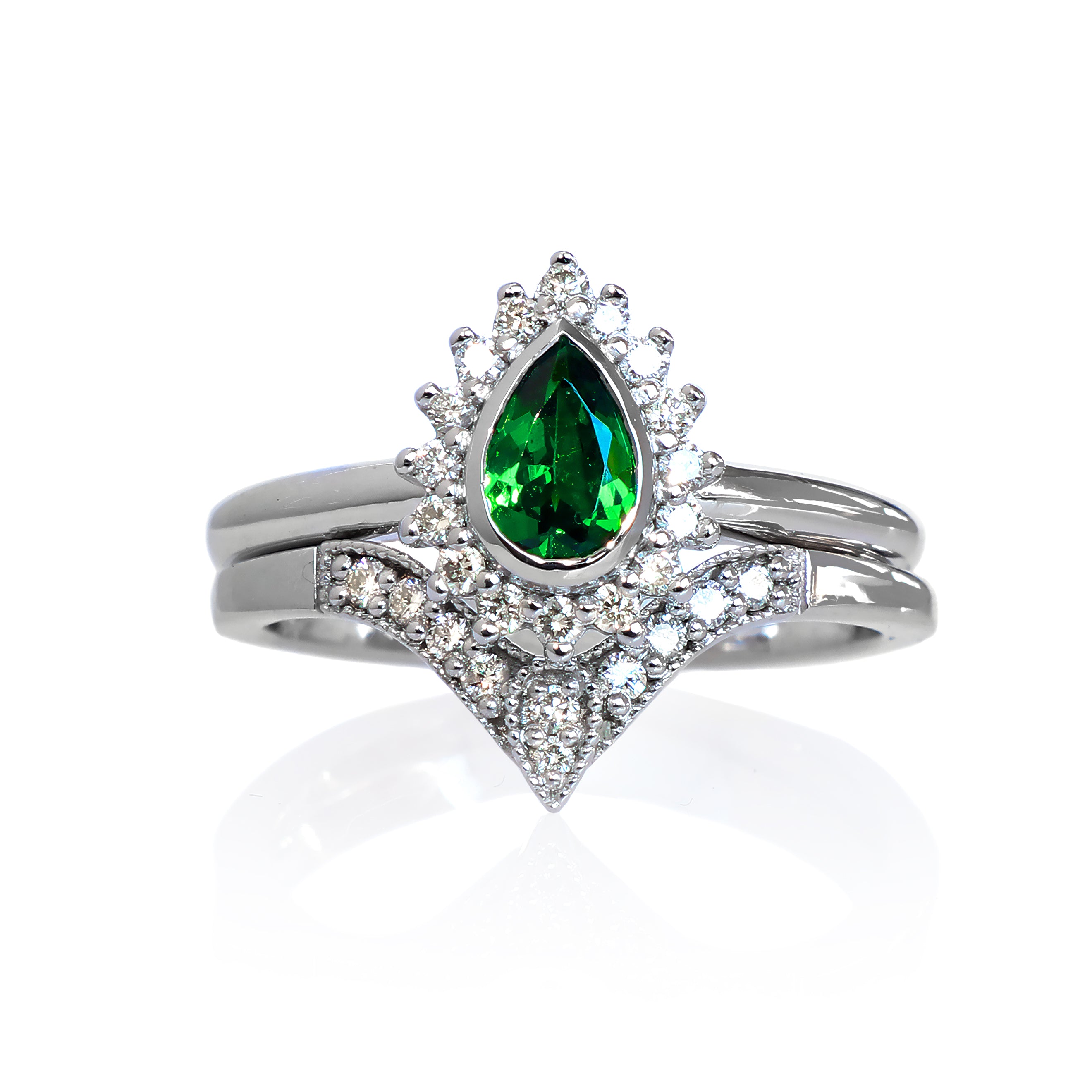 A product photo of a bridal/wedding set made of solid 9k white gold. The engagement ring is made up of a pear-shaped tsavorite gemstone, framed by a halo of diamonds and elegant gold detailing. The band is rounded and smooth, making for comfortable wear. The wedding band is designed to match the engagement ring perfectly, with 10 diamonds embedded along its length to echo the halo that frames the engagement ring's stone. The green gemstone colour would be a good emerald alternative for wearers born in May.