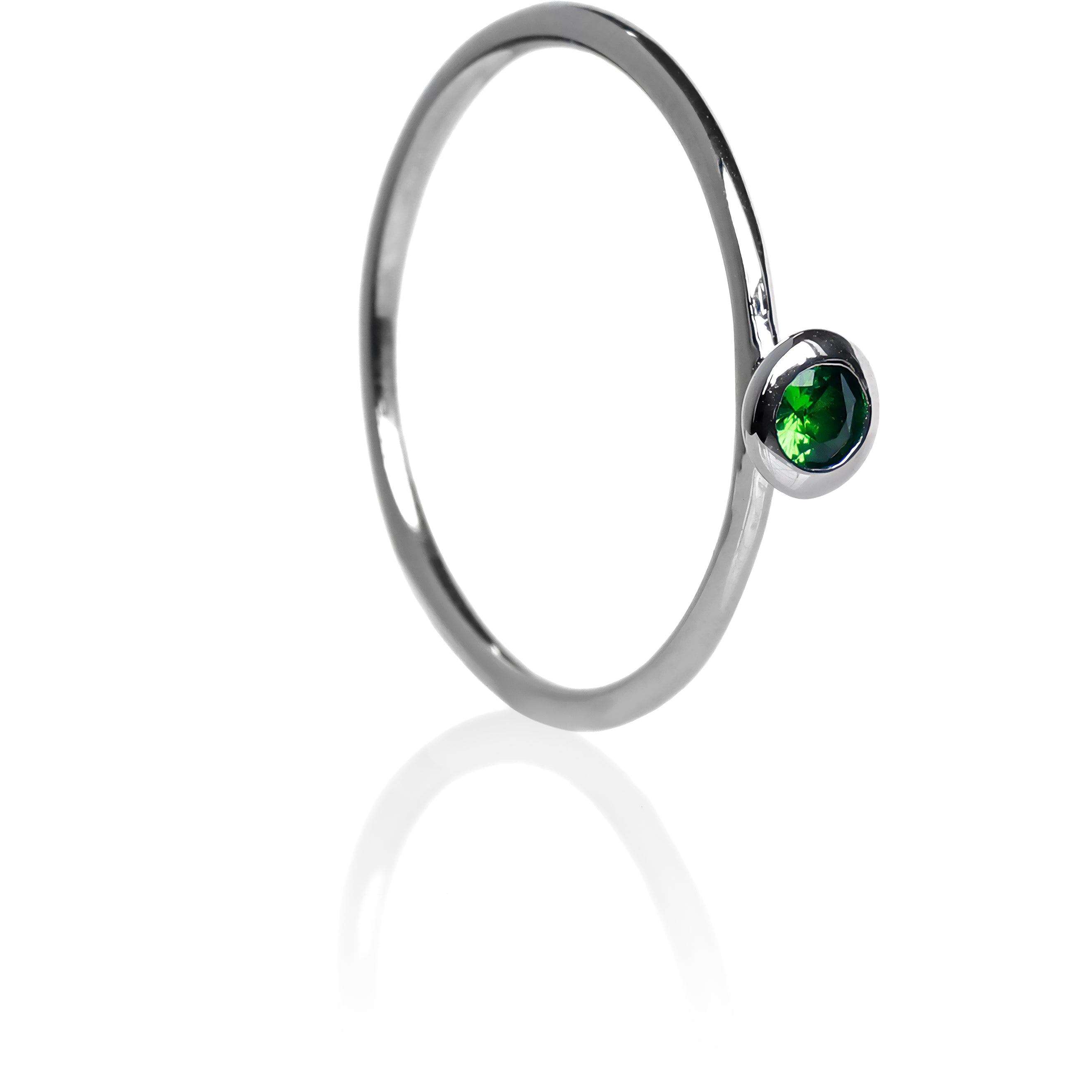 A product photo of a delicate white gold stacking ring with a tiny, bezel-set tsavorite in the centre sitting on a white background. The band is slim and thread-like, with the focus drawn to the petite 3mm glinting green centre stone. The green gemstone colour would be a good emerald substitute.