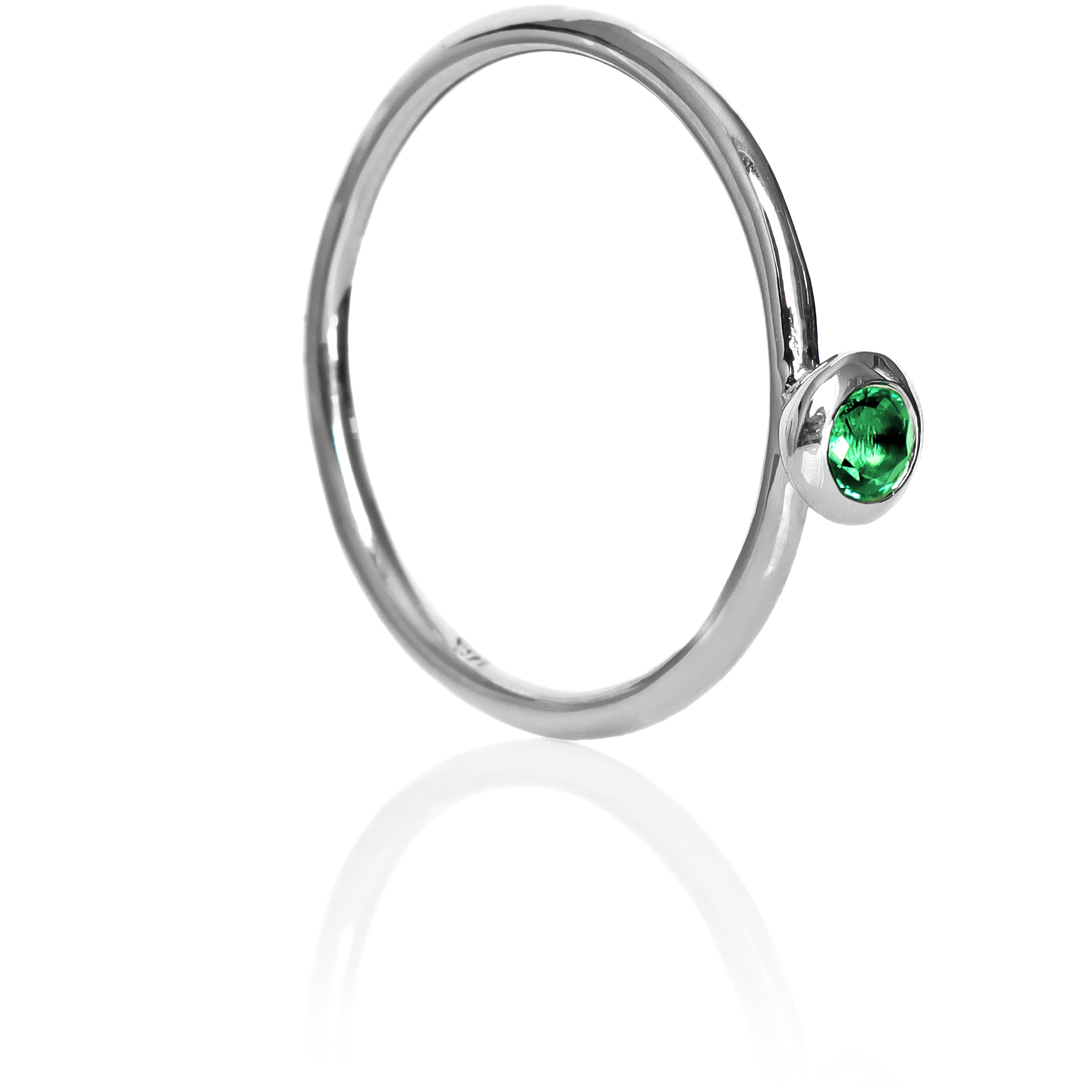 A product photo of a delicate white gold stacking ring with a tiny, bezel-set mint green tourmaline in the centre sitting on a white background. The band is slim and thread-like, with the focus drawn to the petite 3mm glinting green centre stone. The green gemstone colour would be a good emerald substitute.