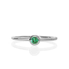 A product photo of a delicate white gold stacking ring with a tiny, bezel-set mint green tourmaline in the centre sitting on a white background. The band is slim and thread-like, with the focus drawn to the petite 3mm glinting green centre stone. The green gemstone colour would be a good emerald substitute.