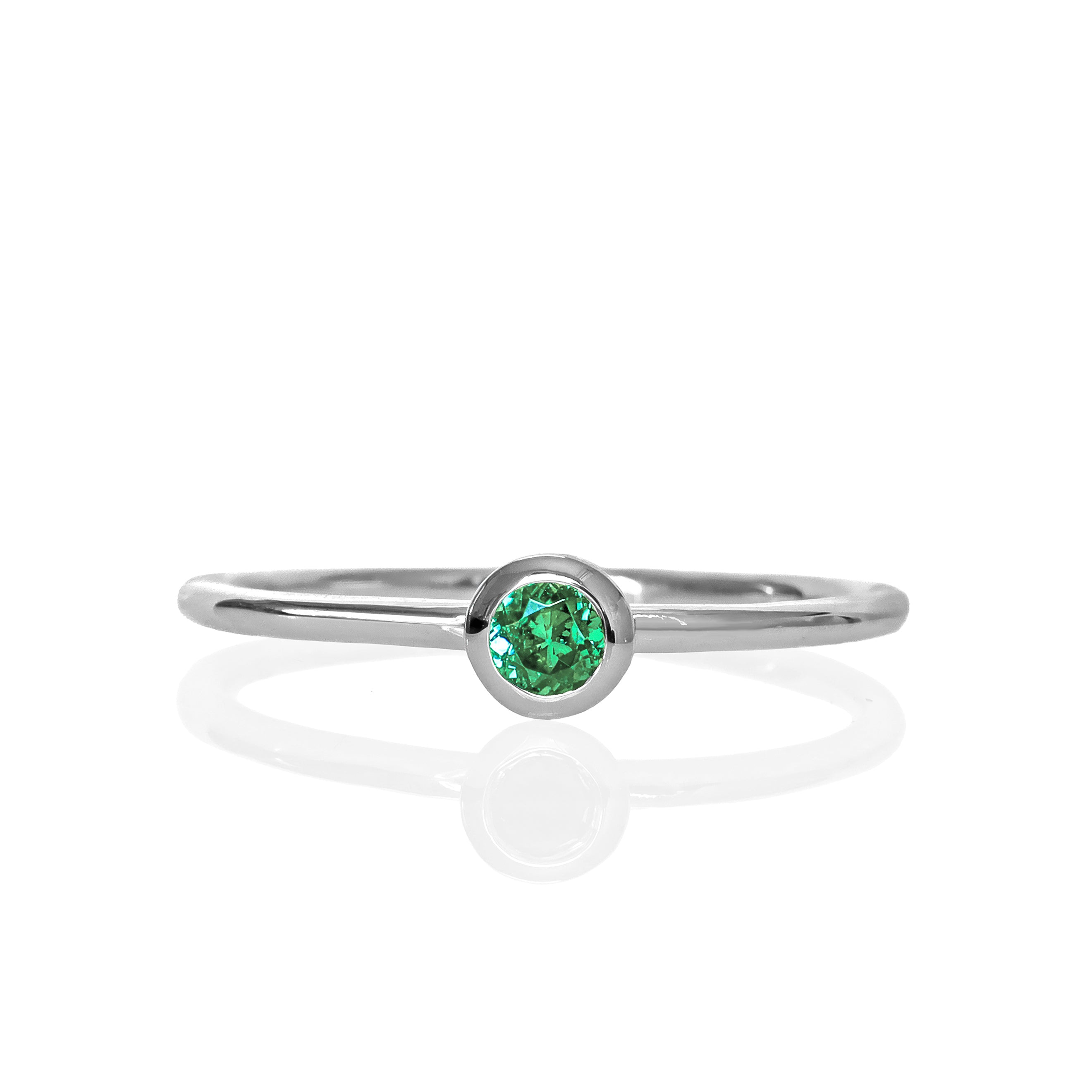 A product photo of a delicate white gold stacking ring with a tiny, bezel-set mint green tourmaline in the centre sitting on a white background. The band is slim and thread-like, with the focus drawn to the petite 3mm glinting green centre stone. The green gemstone colour would be a good emerald substitute.
