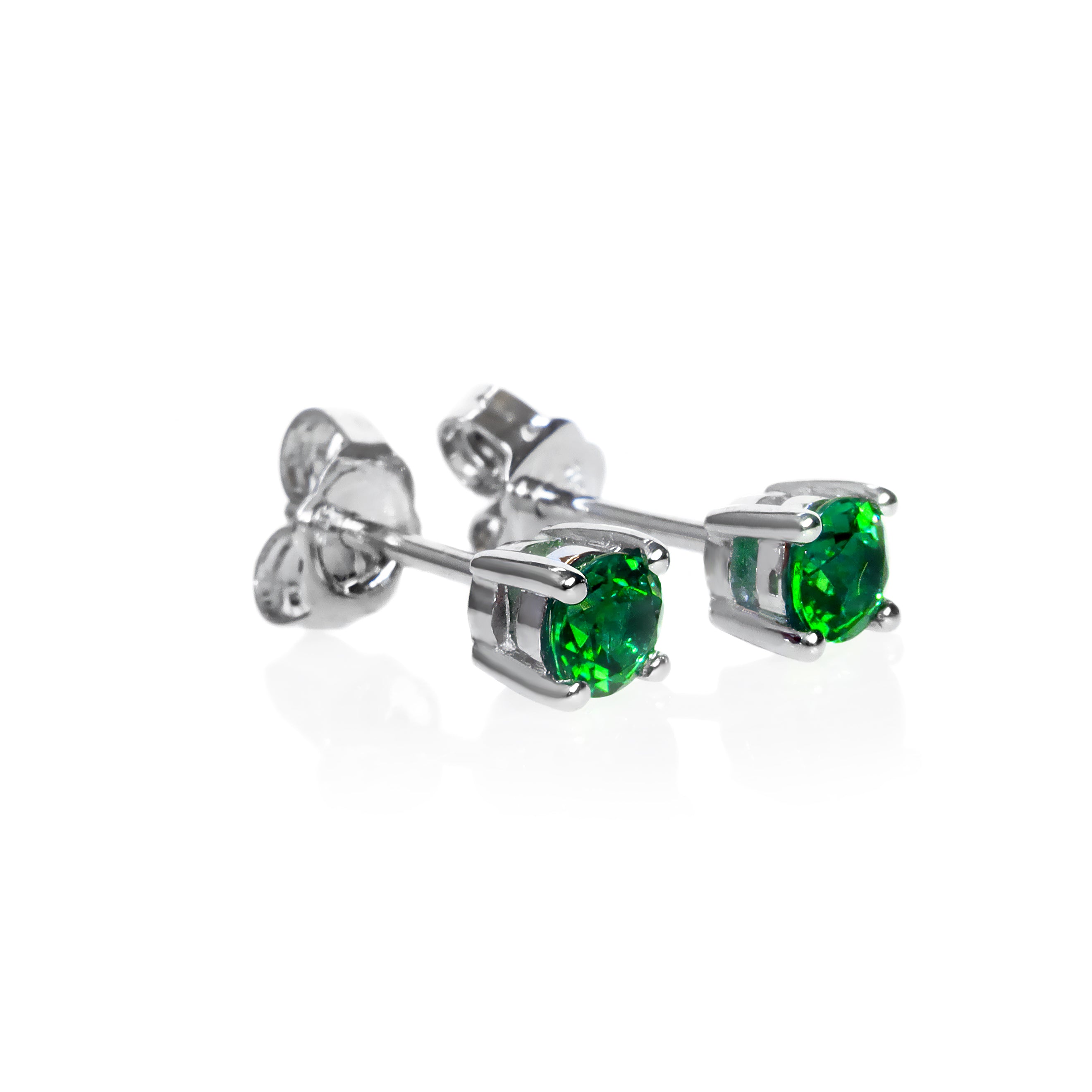 A product photo of two white gold stud earrings sitting on a white background. Held in place by 4 silver claws each are two dazzling round-cut green tsavorite gemstones, reflecting shades of forest-green light from their many edges. The green gemstone colours make these earrings a good alternative or substitute for emerald.