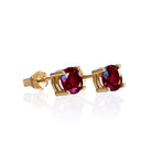 A product photo of two 9 karat yellow gold stud earrings sitting on a white background. Held in place by 4 golden claws each are two dazzling 6mm round-cut rhodalite garnet stones, reflecting violet and plum light from their many edges.