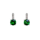 A product photo of a pair of white gold tsavorite earrings sitting against a white background. The simple circle-cut stones are contrasted by the white diamond trio protruding in a straight line above each stone, encased in white gold.