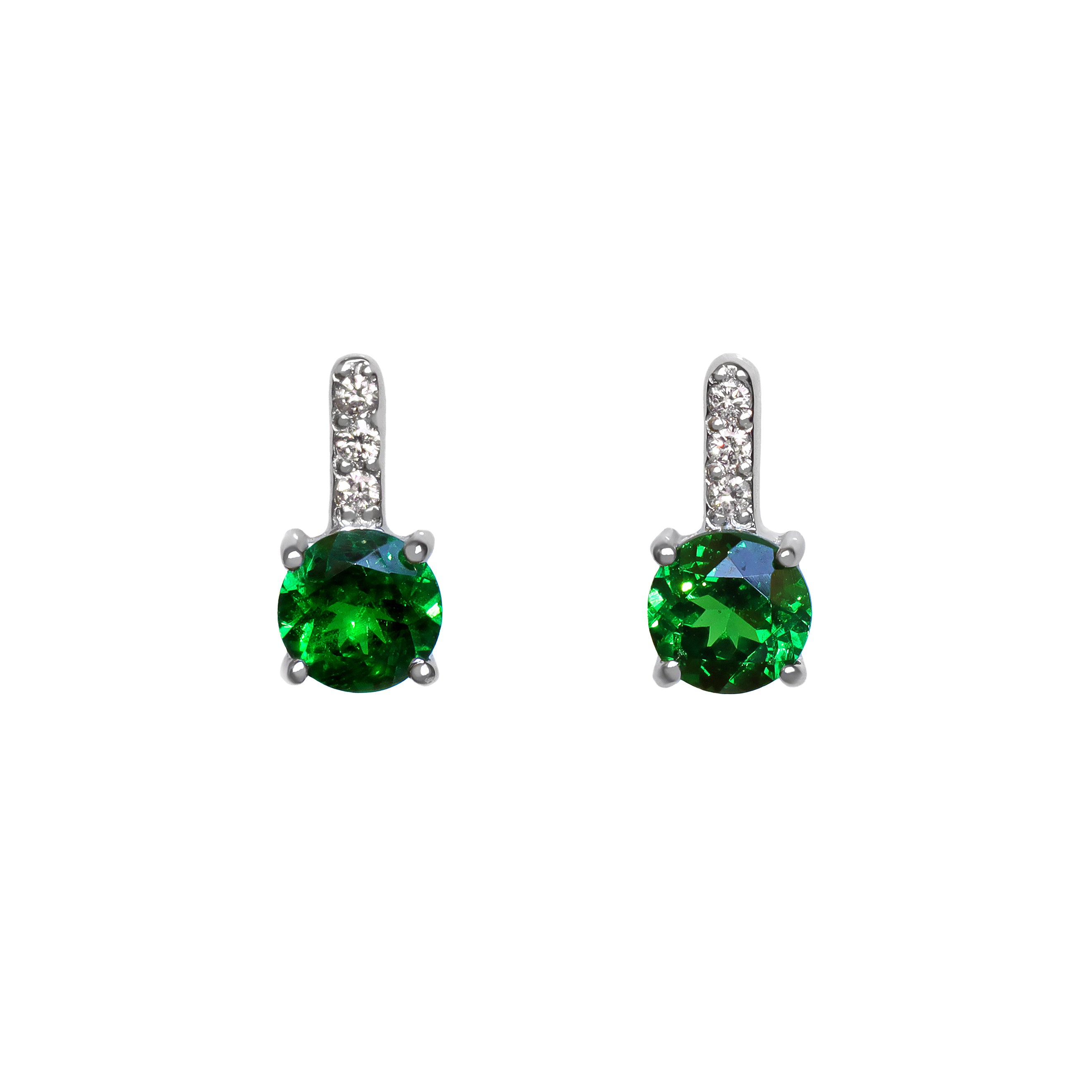 A product photo of a pair of white gold tsavorite earrings sitting against a white background. The simple circle-cut stones are contrasted by the white diamond trio protruding in a straight line above each stone, encased in white gold.