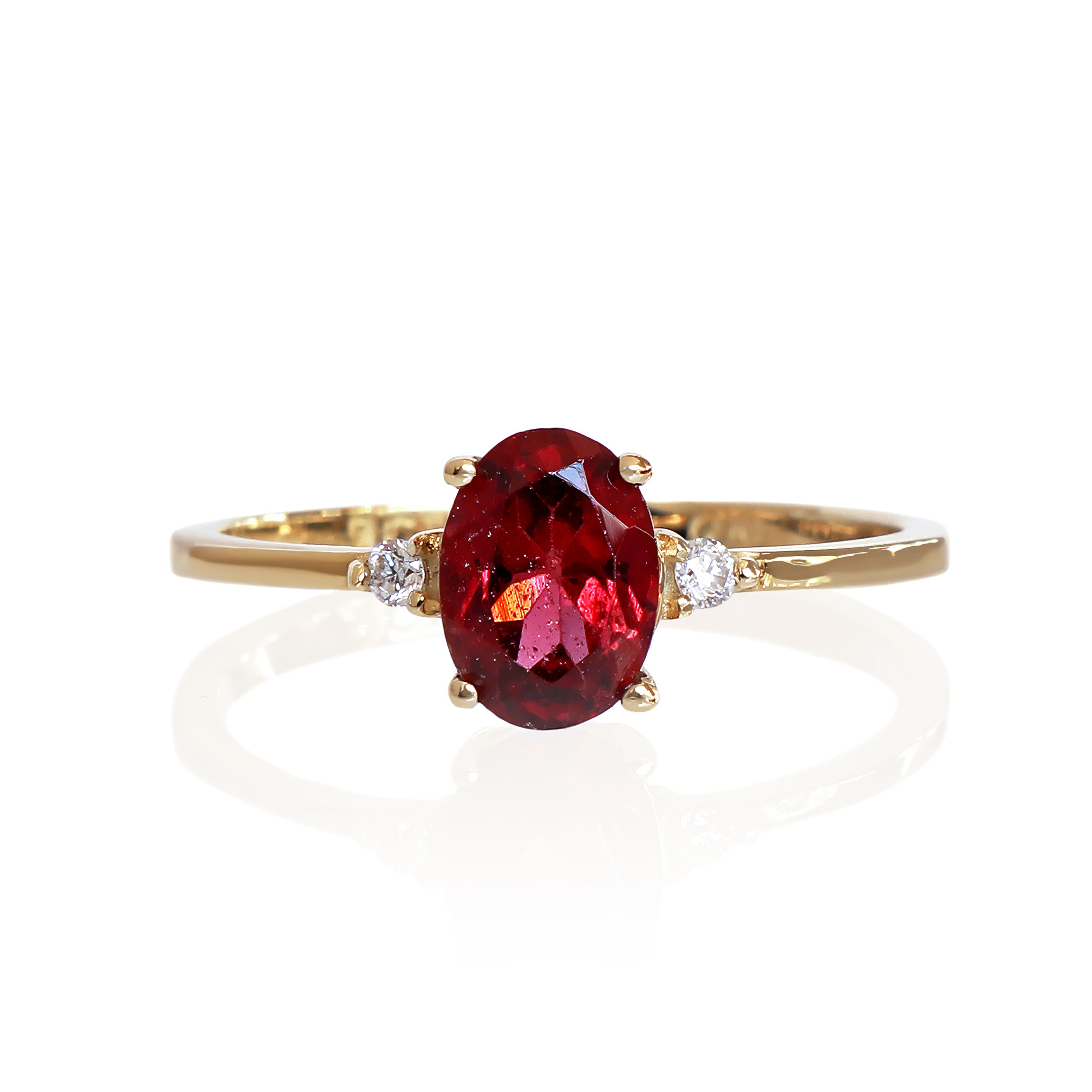 A product photo of a yellow gold red rhodalite ring sitting against a white background. The gold band is plain and smooth, and the centre oval-cut warm reddy pink rhodalite stone is framed by a single white diamond on either side.