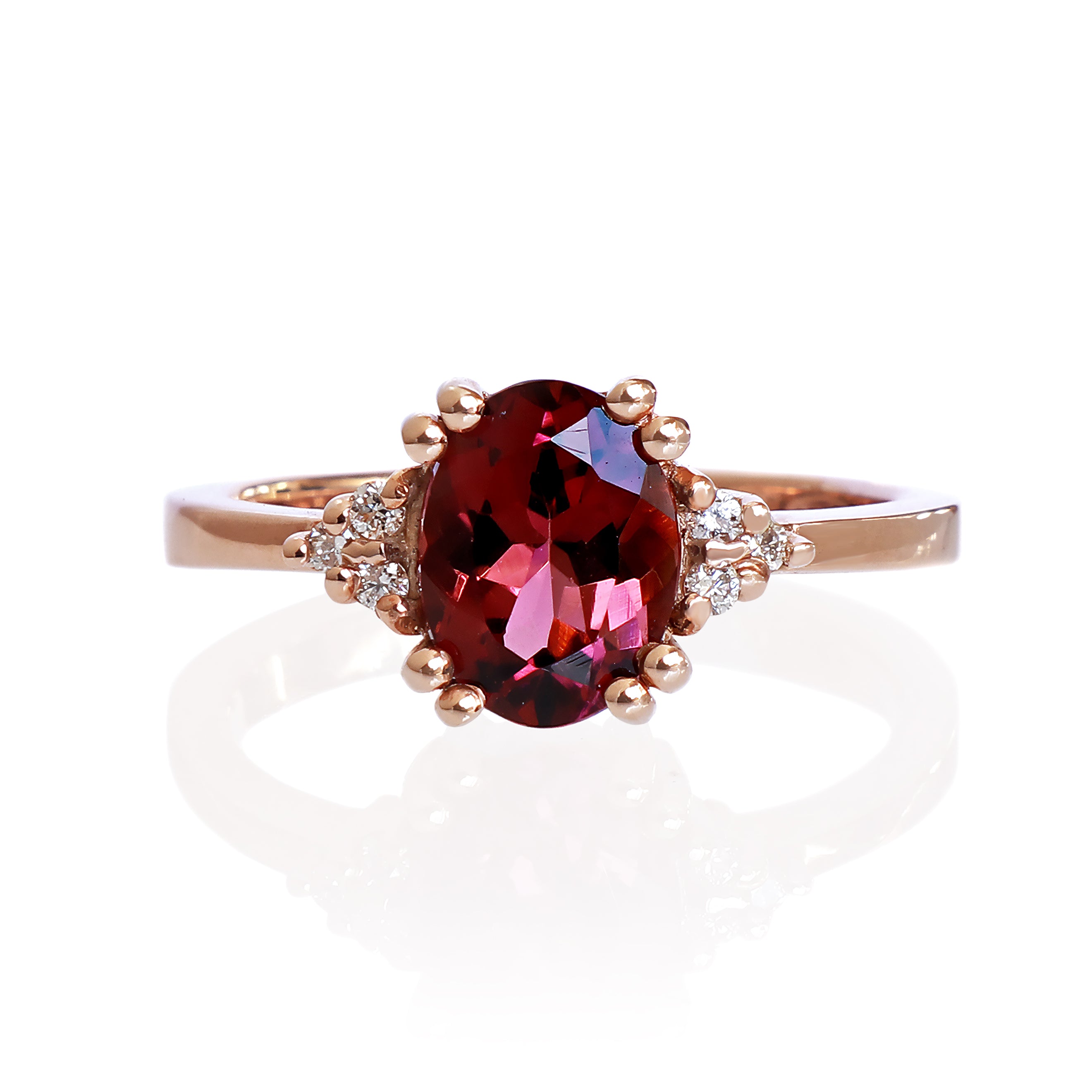 A product photo of a rose gold rhodalite and diamond trio ring sitting on a white background. The oval purple rhodalite gemstone stands in stark contrast to the little clusters of three white diamond stones on either side.
