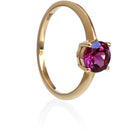 A product photo of a grape garnet solitaire ring in 9 karat solid yellow gold sitting on a white background. The deep purple gemstone measures 6mm across, and reflects breathtaking pink and magenta light from its many faceted edges - in stark contrast to its slim and minimalistic band and simple golden claws.