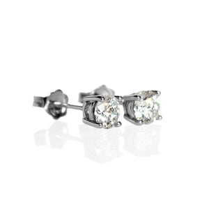 A product photo of a pair of 9 karat white gold lab diamond stud earrings sitting in the sun on a white textured background. The brilliant, colourless half pointer round diamonds measure 5mm across, and are held in place by a simple 4-claw setting.