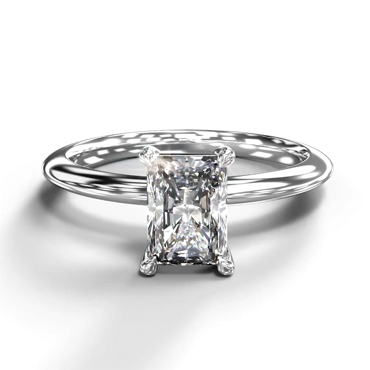 A turntable video of a 14 karat white gold lab diamond engagement ring sitting in the sun on a white textured background. The brilliant, colourless 1ct emerald-cut diamond measures about 6.7mm lengthwise, and is held in place by 4 delicate golden claws in a prong setting.