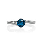 A product photo of a curved-band silver solitaire ring with an ocean blue London Blue Topaz centre stone sitting on a white background. The deep blue gemstone colour would be a good sapphire substitute.
