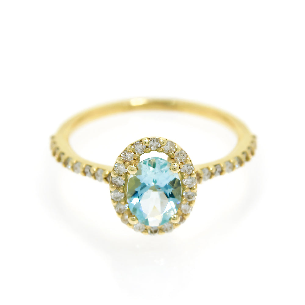A product photo of an aquamarine ring in 9 karat yellow gold on a white background. A large, brilliant oval jewel in the centre reflects pale baby blue-coloured light, and is framed by a ring of white diamonds. A simple round band continues the diamond detailing for half of its length, smoothing out into a simple yellow gold back.