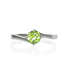 A product photo of a curved-band silver solitaire ring with a grass green peridot centre stone sitting on a white background.