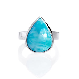 A product photo of a silver Larimar ring on a white background. The band is tall and thick. The 16x12mm pear cabochon Larimar stone has dappled white and light blue patterning, similar to water reflections at the bottom of a pool. The stone is set in a thick silver bezel setting.