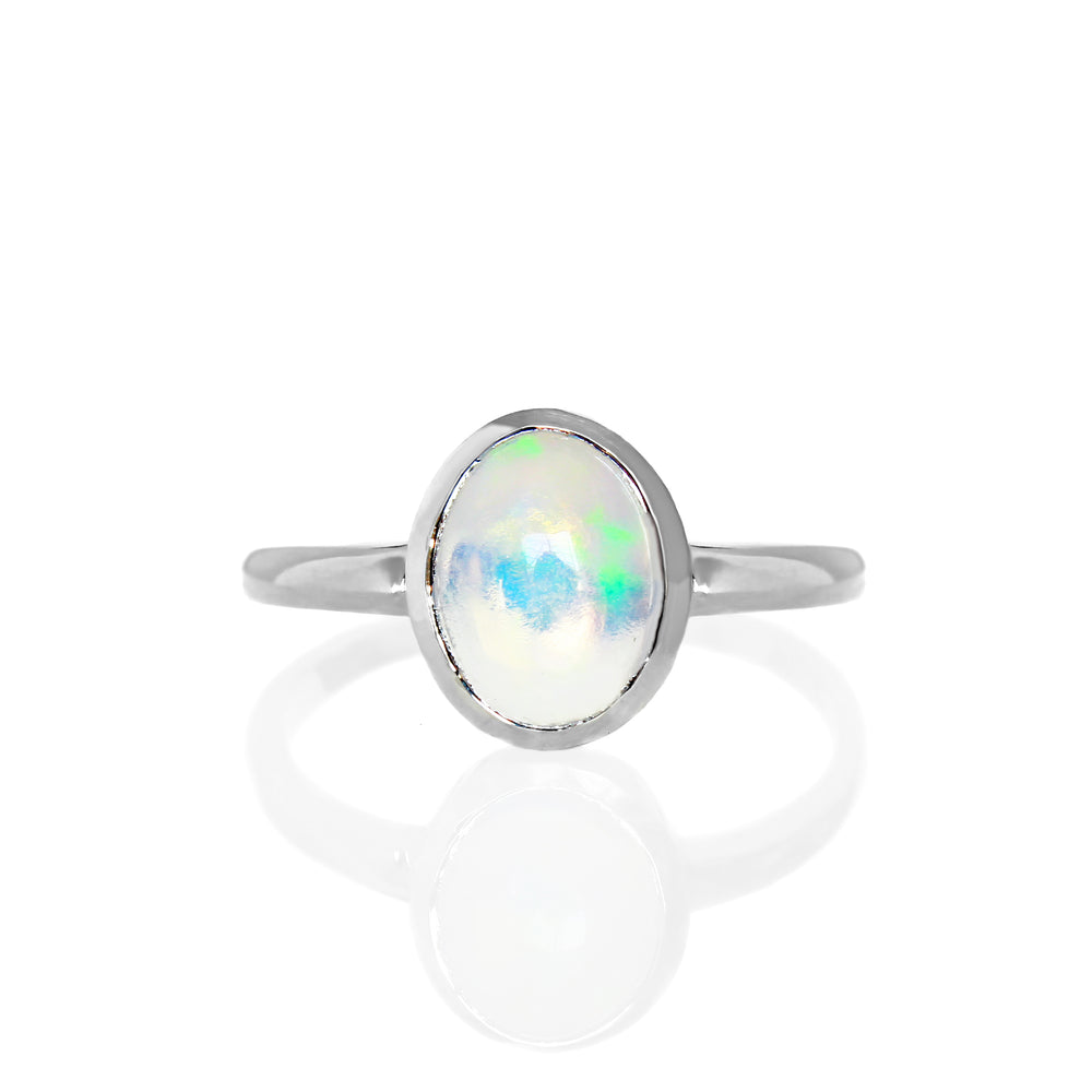 A product photo of a silver rainbow opal ring on a white background. The band is tall and thick. The 9x7mm oval cabochon opal stone is uniquely translucent, with a moonstone-like sheen and rainbow-coloured fire. The stone is set in a thick silver bezel setting.