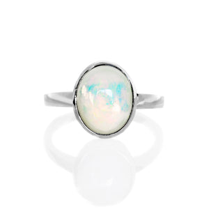 A product photo of a silver rainbow opal ring on a white background. The band is tall and thick. The 10x8mm oval cabochon opal stone is uniquely translucent, with a moonstone-like sheen and rainbow-coloured fire. The stone is set in a thick silver bezel setting.