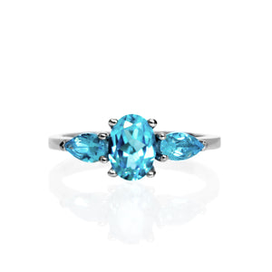 A product photo of a dainty and elegant white gold ring with a stunning trio of blue topaz jewels sitting against a white background. The largest of the stones sits in the centre, a 7x5mm swiss blue topaz - hugged by two smaller pear-shaped sky blue topaz stones on either side.