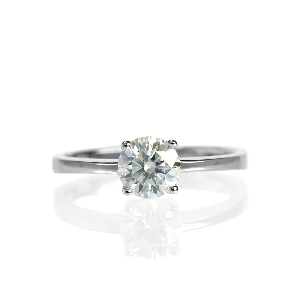 A product photo of a Round moissanite Solitaire Ring set in solid 9 karat white gold sitting on a plain white background. The moissanite centrestone measures 5.5mm across. The sparkling clear moissanite centre stone is held in place by 4 claws and reflects light off of its many facets. The brilliance would make it a good diamond substitute.