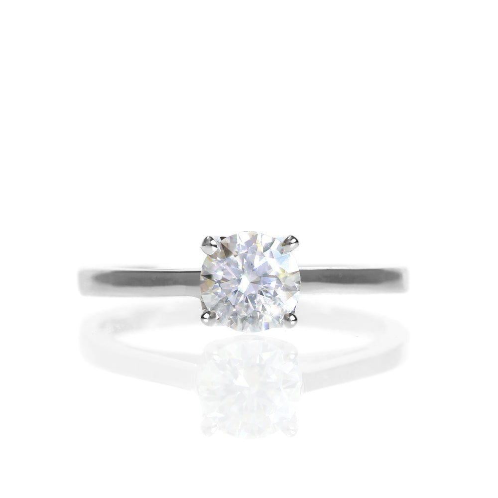 A product photo of a simple moissanite solitare ring set in solid 9k white gold sitting on a white background. The face of the ring is deceptively simple, appearing like a standard solitare ring, but with hidden cathedral style supports and a stylised floral backing connecting the stone to the band.