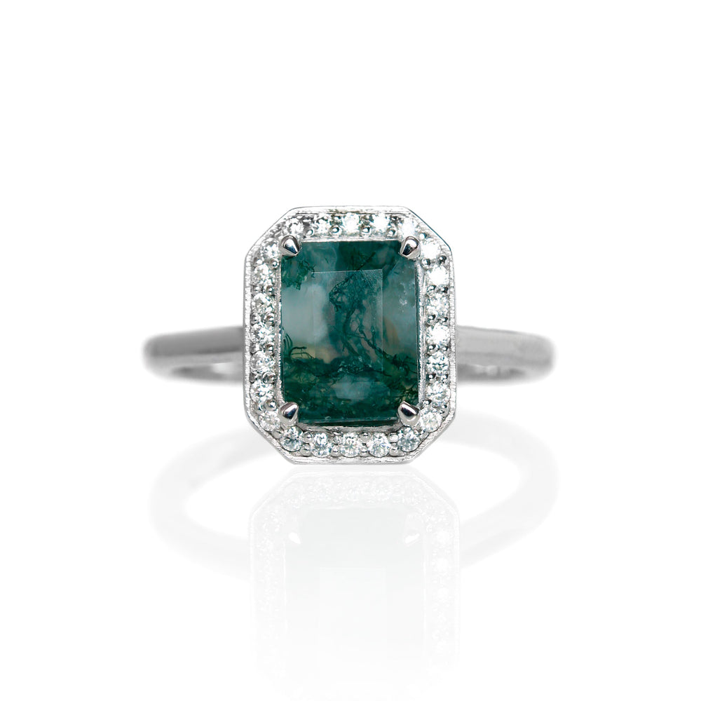 A product photo of a lavish moissanite halo moss agate ring in solid sterling silver on a white background. The smooth band meets the octagonal halo and moss agate in the centre. The impressively large moss agate centre stone is held in place by 4 claws and is heavily included, with natural mossy swirls and strikes snaking throughout the green jewel.