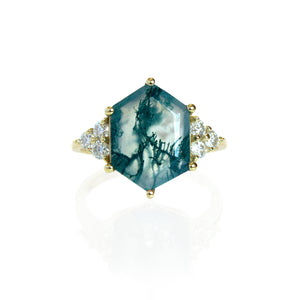 A product photo of a statement diamond and moss agate engagement ring in solid gold sitting on a white background. The band is smooth and rounded. The impressively large 14x10mm Hexagonal Moss Agate gemstone is embraced on either side by a delicate trio of bright, natural diamonds.