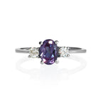 A product photo of a faceted lab alexandrite and moissanite ring in solid sterling silver on a white background. The faceted cut of the lab-grown alexandrite allows for its sparkling appearance to shine, while the round faceted moissanites add a burst of sparkling rainbow fire to the ring.