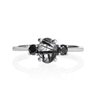 A product photo of a faceted Tourmalated Quartz and black moissanite ring in solid sterling silver on a white background. The faceted cut of the tourmalated stone allows the viewer to see every angle of the needle-like inclusions within, while the black diamonds echo the dark colouring of the centre stone.