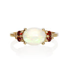A product photo of a solid 9 carat yellow gold Ethiopian Rainbow Opal and natural diamond/garnet trio cluster ring sitting on a white background. The large oval rainbow opal stands in stark contrast to the little clusters of 2 white sparkling diamond stones on either side.