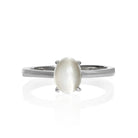 A product photo of an oval 925 sterling silver solitaire ring on a white background. The band is rounded and smooth, and the 7x5mm cabochon grey moonstone birthstone is held in place by 4 delicate silver claws.